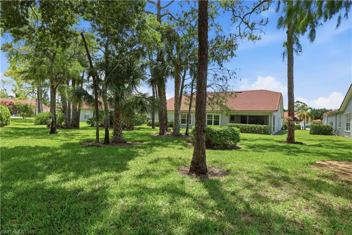 Expansive green lawn with mature trees and palm trees providing natural shade