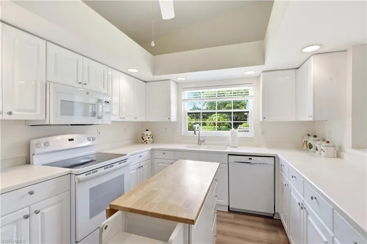 Bright kitchen featuring extensive white cabinetry, light countertops, wood-finish flooring, recessed lighting, and a window over the sink