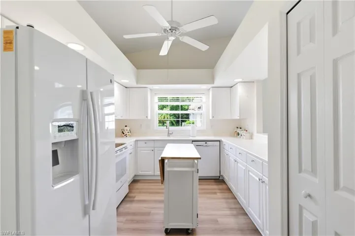 Bright kitchen featuring white cabinetry, light countertops, wood-finish flooring, a vaulted ceiling with a ceiling fan, and recessed lighting