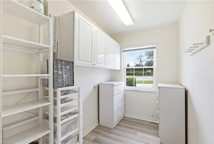 Bright room featuring a window overlooking greenery, overhead cabinetry, and wood-finish flooring