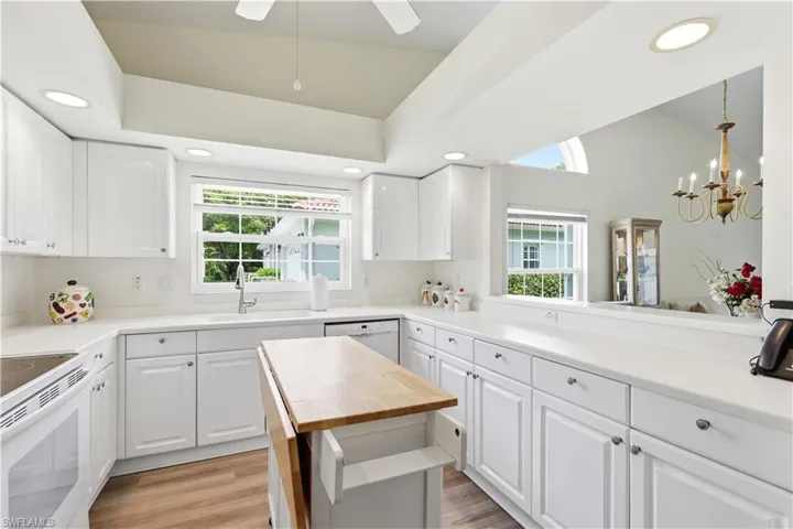 Spacious kitchen featuring white cabinetry, light countertops, wood-finish flooring, recessed lighting, and a pass-through window to the adjacent room