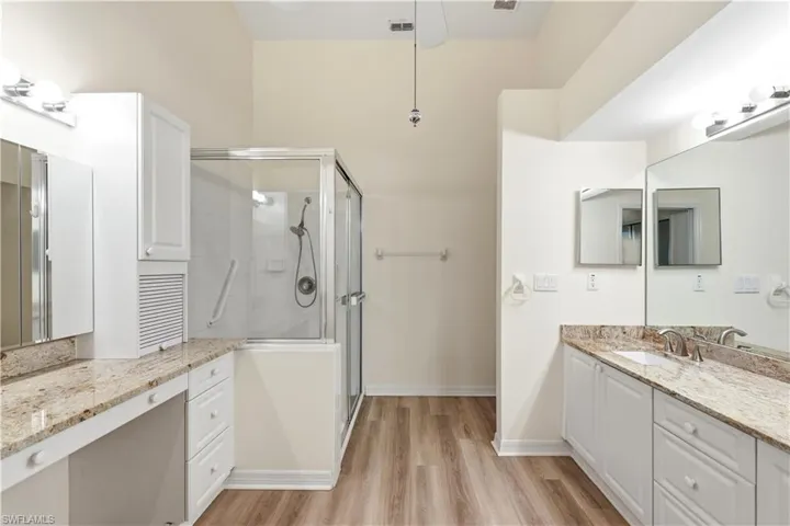 Spacious bathroom featuring a glass-enclosed shower, dual vanity with undermount sinks, stone countertops, and wood-finish flooring