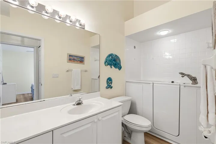 Bathroom featuring a walk-in tub with tile surround, a single vanity with an integrated sink, and wood-finish flooring