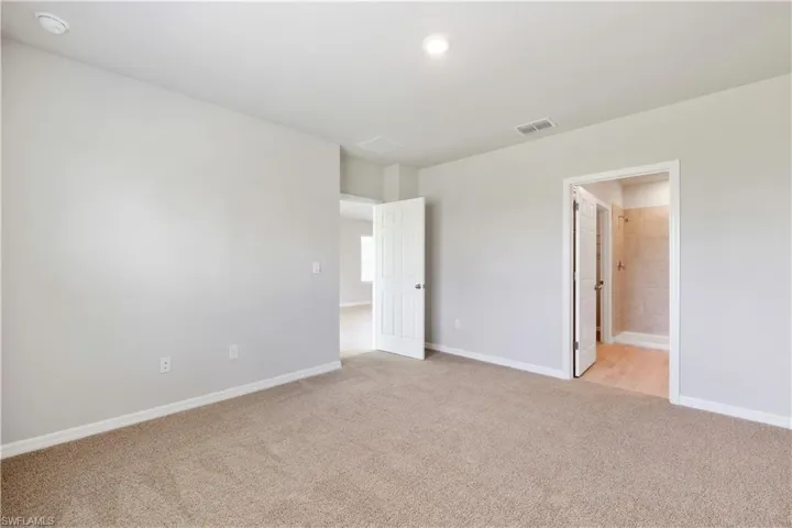 Unfurnished bedroom featuring light carpet and connected bathroom