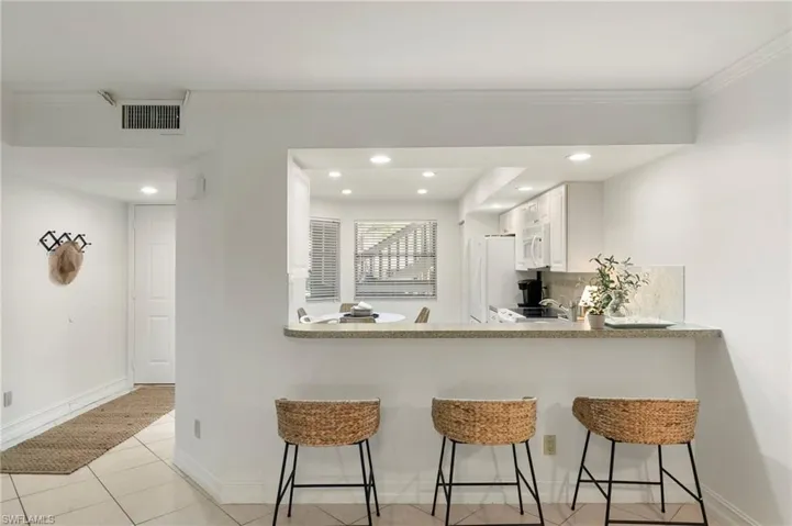 Kitchen featuring a kitchen bar, white cabinets, light countertops, light tile patterned floors, and a peninsula