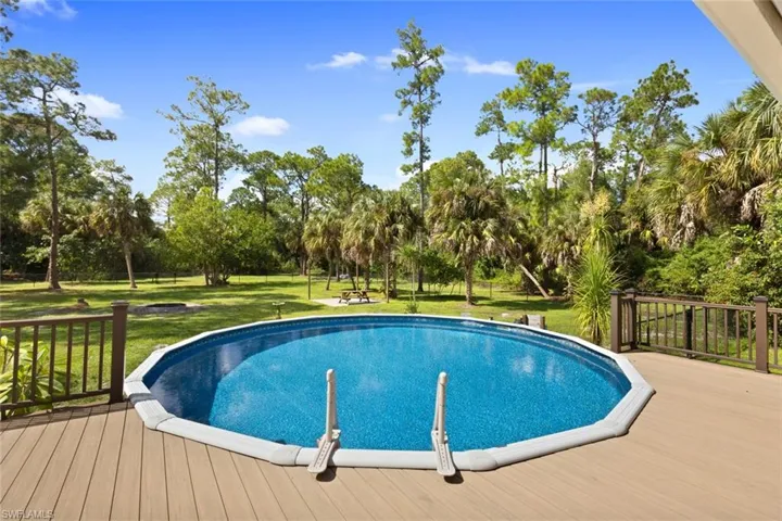 Swimming pool with a lawn, a wooden deck, and view of scattered trees