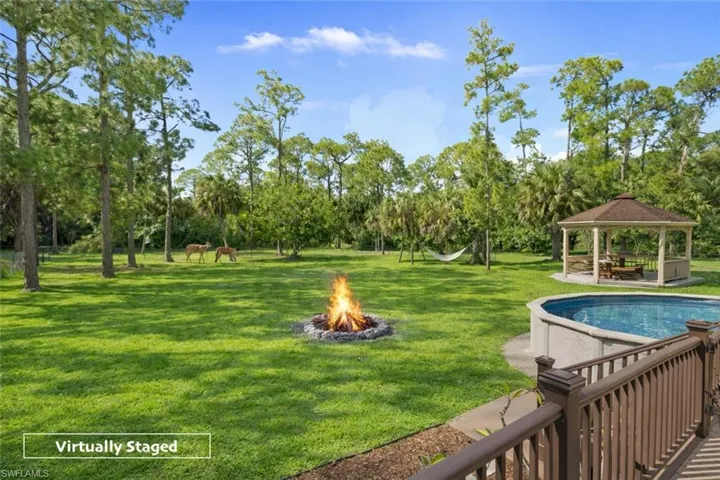 View of green lawn featuring a fire pit, a gazebo, an outdoor pool, a patio, and view of wooded area