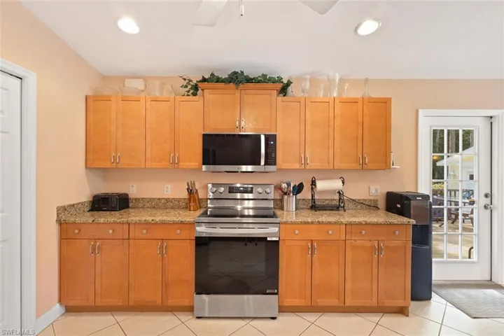 Kitchen featuring appliances with stainless steel finishes, light stone counters, light tile patterned flooring, recessed lighting, and brown cabinets