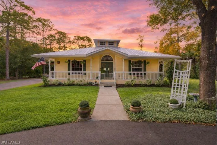 Farmhouse inspired home featuring a metal roof, covered porch, a front yard, and driveway
