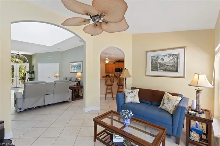 Living area with a ceiling fan, light tile patterned floors, arched walkways, and french doors