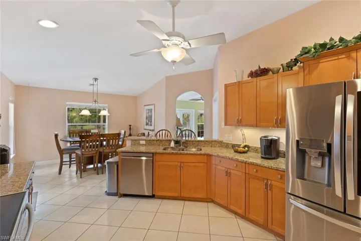 Kitchen featuring appliances with stainless steel finishes, a peninsula, brown cabinetry, light stone counters, and light tile patterned floors