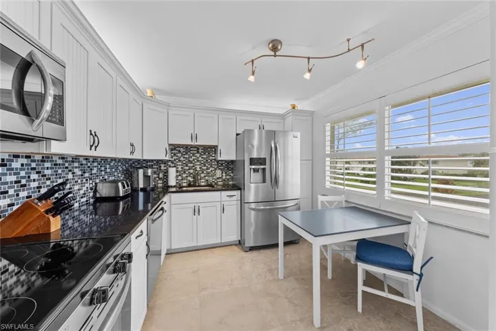 Kitchen with decorative backsplash, dark stone counters, ornamental molding, stainless steel appliances, and white cabinets