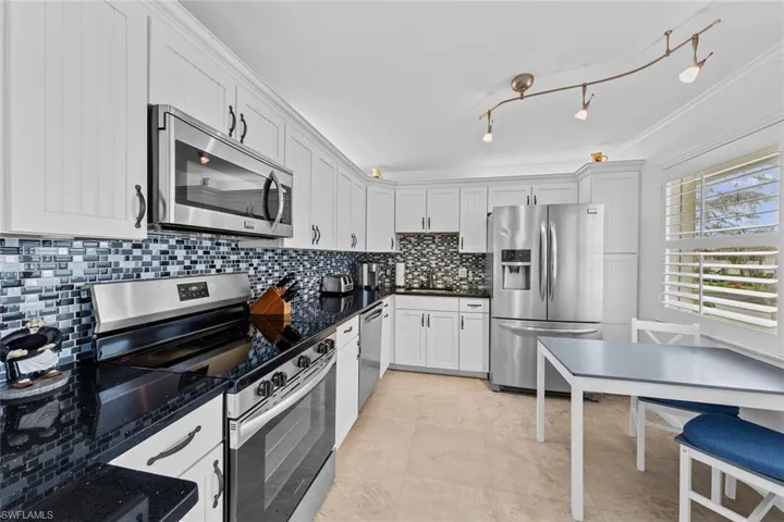 Kitchen with dark stone counters, crown molding, decorative backsplash, white cabinetry, and stainless steel appliances