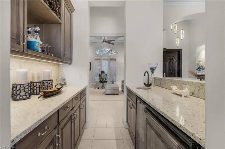 Kitchen with crown molding, dark brown cabinets, ceiling fan, light stone counters, and light tile patterned flooring