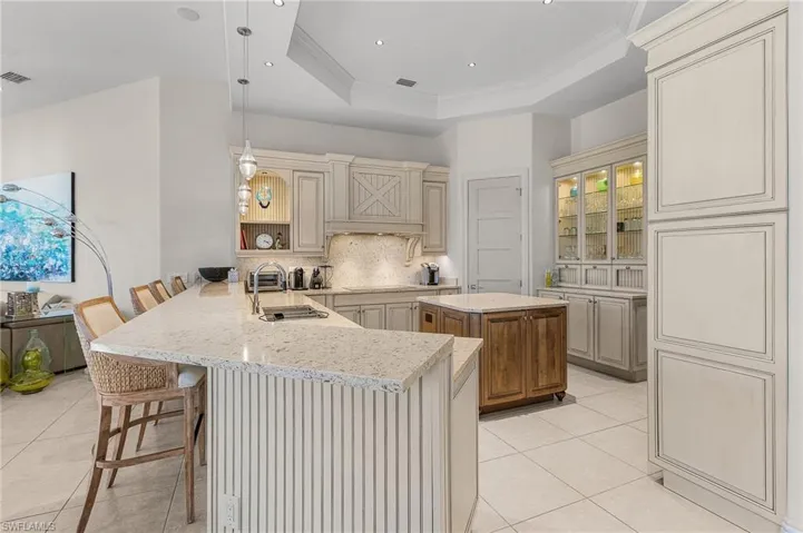 Kitchen featuring kitchen peninsula, pendant lighting, sink, backsplash, and a breakfast bar