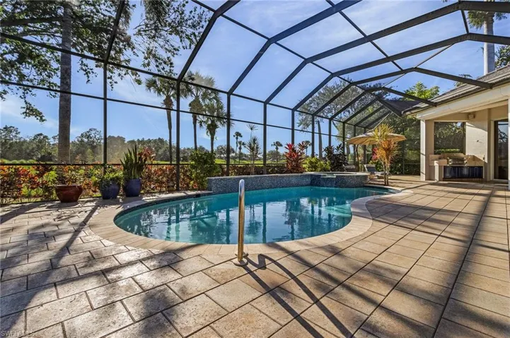 View of pool featuring glass enclosure, an outdoor kitchen, and a patio