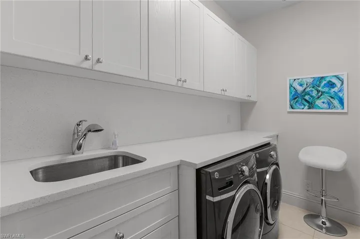 Laundry area with cabinets, sink, washer and clothes dryer, and light tile patterned flooring