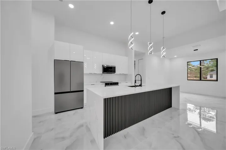 Kitchen with stainless steel appliances, light marble finish flooring, hanging light fixtures, modern cabinets, and white cabinets