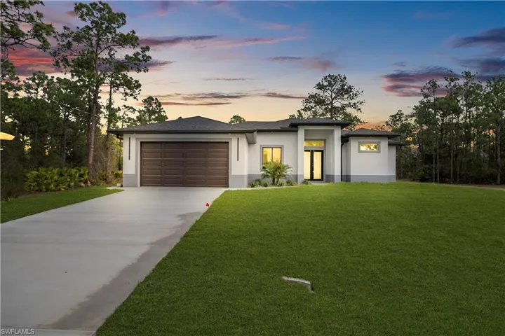 Prairie-style house featuring a front lawn, a garage, stucco siding, and concrete driveway