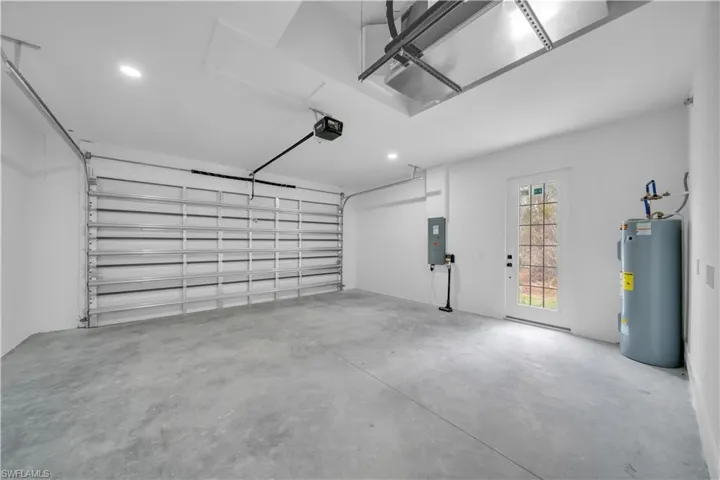 Garage with electric water heater, electric panel, recessed lighting, and a garage door opener