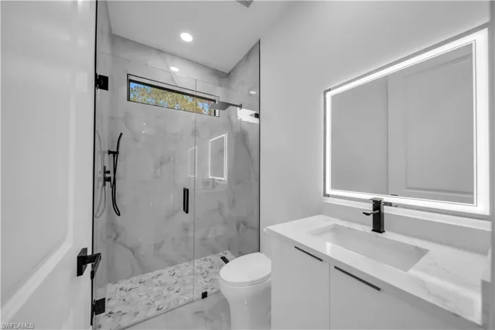 Bathroom with a marble finish shower, vanity, and recessed lighting