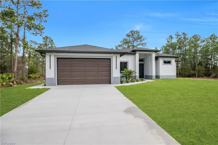 Prairie-style home featuring a front yard, stucco siding, an attached garage, and driveway