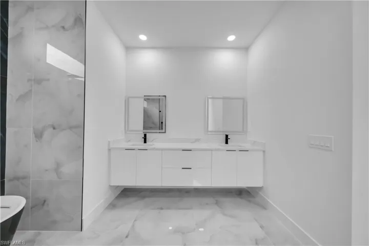 Bathroom with double vanity, recessed lighting, and light marble finish flooring
