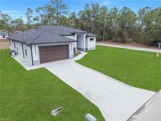 View of front of house with a front yard, roof with shingles, concrete driveway, a garage, and stucco siding