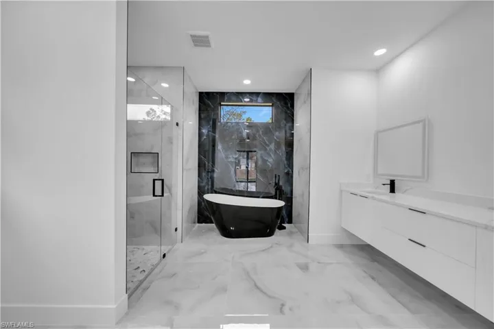 Bathroom featuring a marble finish shower, a freestanding tub, vanity, recessed lighting, and light marble finish floors