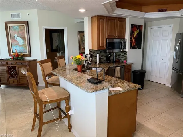 Kitchen featuring a kitchen breakfast bar, light stone counters, a peninsula, appliances with stainless steel finishes, and tasteful backsplash