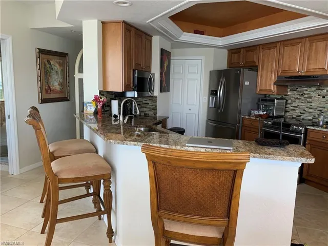 Kitchen featuring brown cabinetry, a kitchen breakfast bar, a peninsula, light tile patterned floors, and backsplash