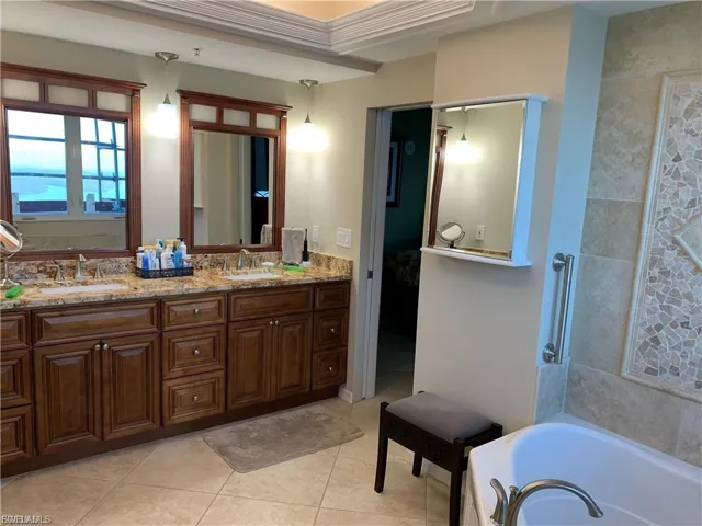 Ensuite bathroom with a bath, double vanity, and light tile patterned flooring