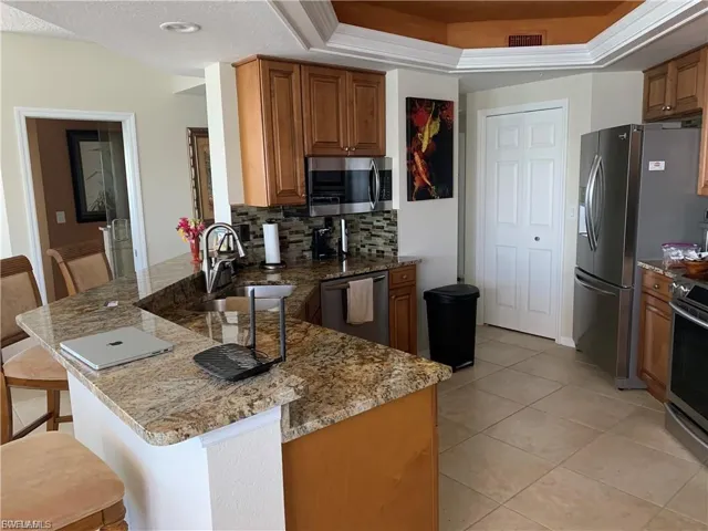 Kitchen featuring a peninsula, a breakfast bar area, light stone counters, and brown cabinets