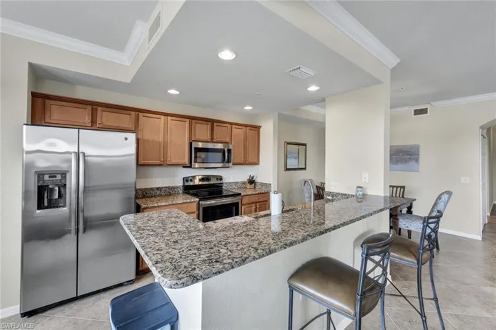 Kitchen with crown molding, a kitchen breakfast bar, stainless steel appliances, brown cabinetry, and dark stone counters