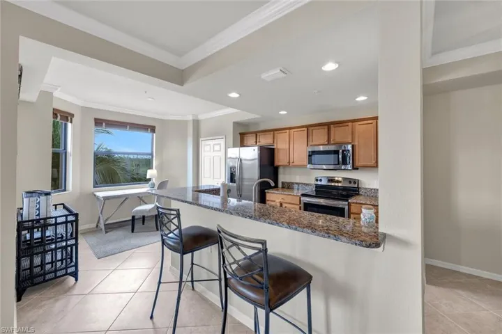 Kitchen featuring a kitchen bar, crown molding, dark stone countertops, appliances with stainless steel finishes, and light tile patterned floors