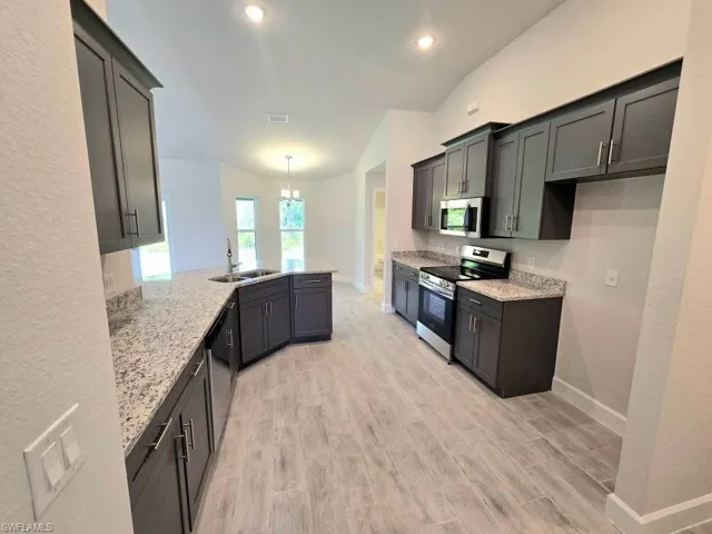 Kitchen with appliances with stainless steel finishes, a sink, a peninsula, baseboards, and recessed lighting