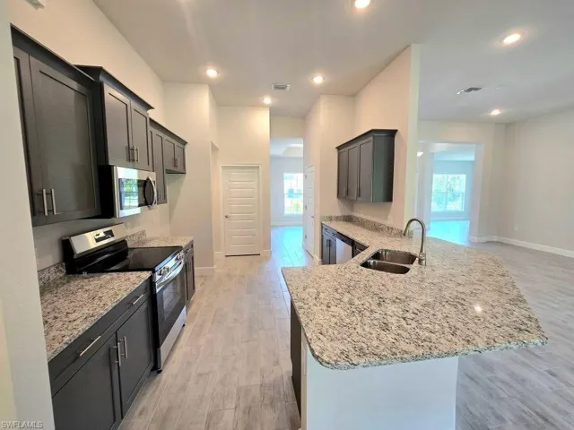 Kitchen with stainless steel appliances, a sink, light stone counters, a peninsula, and recessed lighting