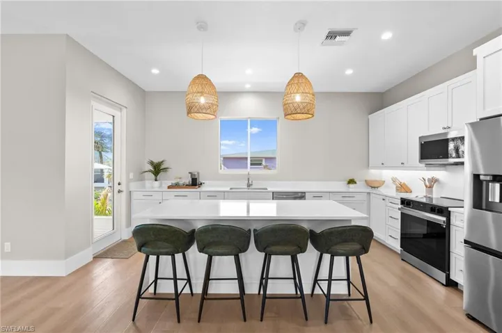 Entertainers Kitchen with a sink, stainless steel appliances, light wood finished floors, a kitchen bar, and visible vents - virtually edited photo