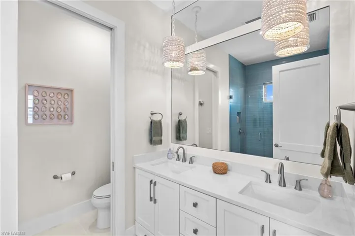 Bathroom with toilet, double sinks, tile patterned floors, and a stall shower. virtually edited photo
