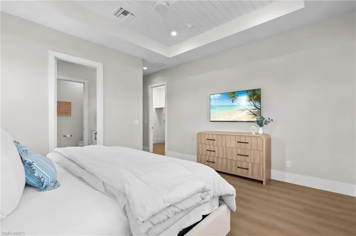 Bedroom with a raised ceiling, wooden ceiling, light wood-type flooring, and baseboards. virtually edited photo