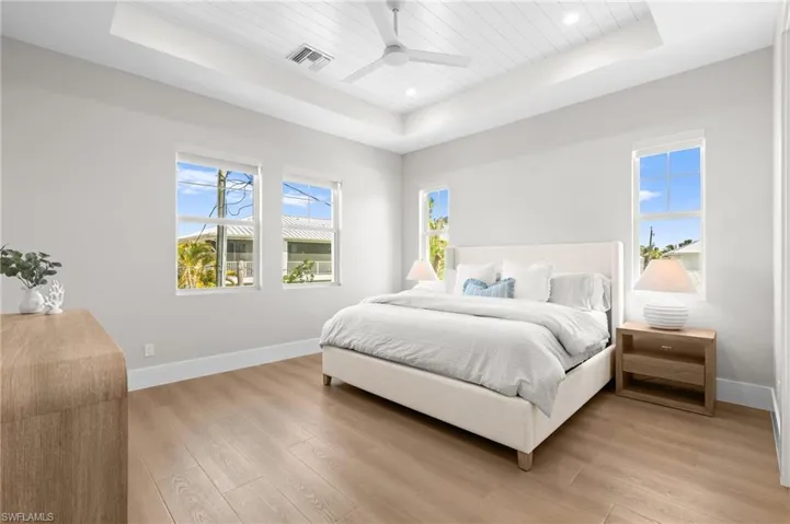 Bedroom with visible vents, baseboards, light wood-style floors, and a raised ceiling. virtually edited photo