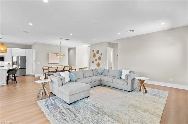 Living area with baseboards, light wood finished floors, visible vents, and recessed lighting. virtually edited photo