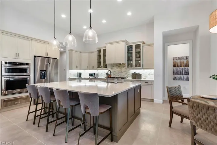 Kitchen with glass fronted cabinets, a spacious island, hanging light fixtures, and light stone countertops