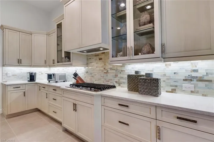 Kitchen featuring light stone countertops, light tile patterned floors, tasteful backsplash, and glass fronted cabinets