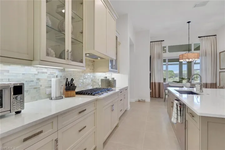 Kitchen featuring glass insert cabinets, light stone counters, decorative light fixtures, stainless steel appliances, and decorative backsplash