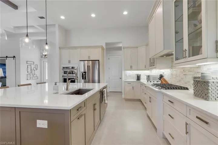 Kitchen with glass fronted cabinets, light stone countertops, a barn door, pendant lighting, and stainless steel appliances