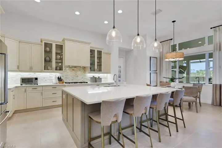 Kitchen with glass fronted cabinets, decorative light fixtures, a spacious island, light stone countertops, and two tone cabinetry