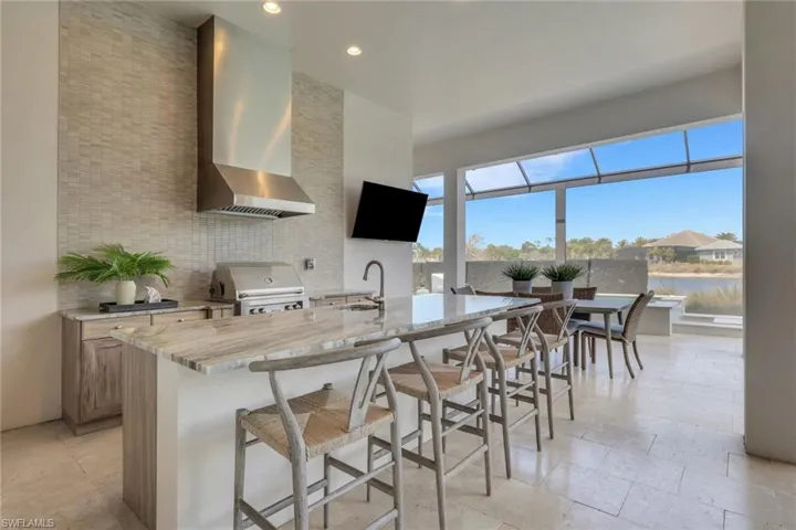 Kitchen with a sunroom, light stone counters, a kitchen island with sink, a kitchen breakfast bar, and backsplash