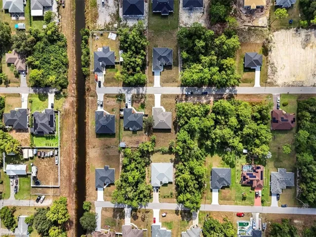 Aerial perspective of a residential neighborhood featuring paved streets, established tree cover, concrete driveways, and proximity to a linear canal