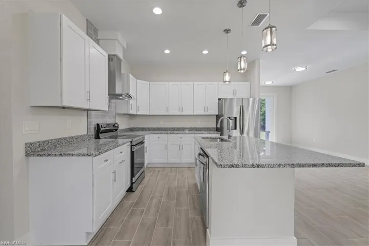 Kitchen featuring white shaker-style cabinetry, stone-surface countertops, wood-finish tile flooring, stainless steel appliances, and glass pendant lighting